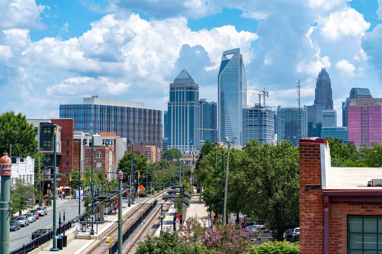Panoramic view of Charlotte's cityscape with a clear blue sky and fluffy clouds overhead, featuring the light rail tracks in the foreground